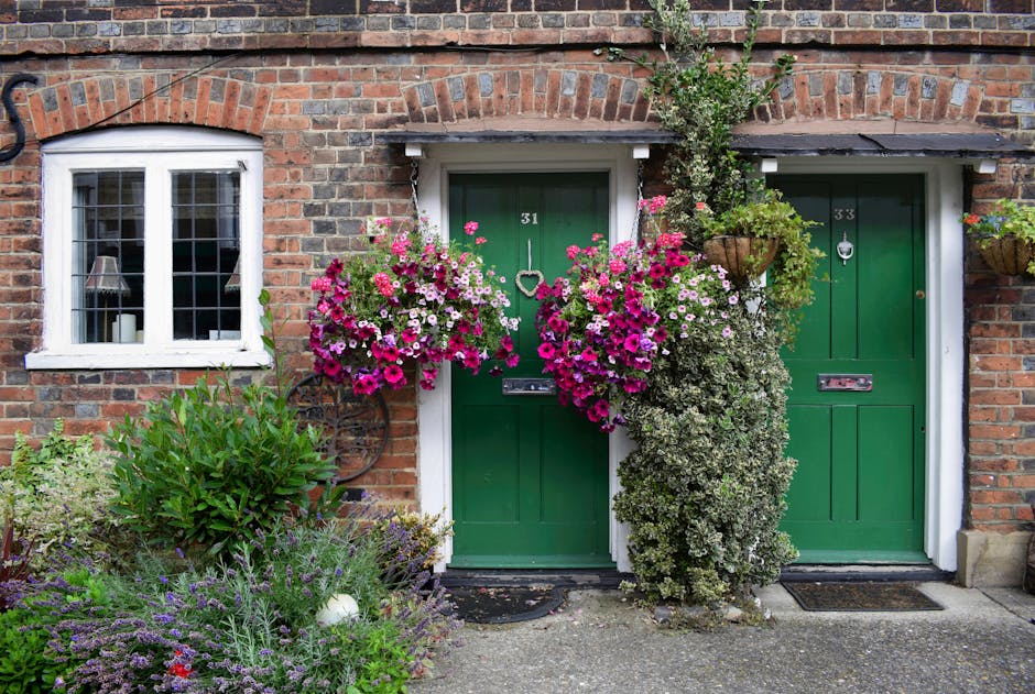 The image depicts a charming front garden of a brick house in Carshalton, showcasing well-maintained garden beds with a variety of plants, including lavender and leafy shrubs, arranged along the paved