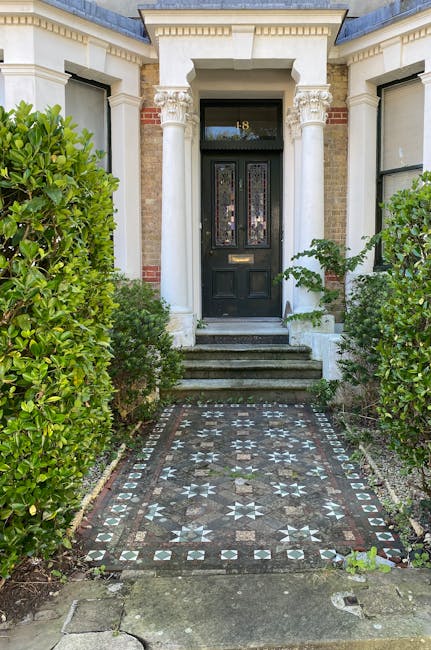 The image depicts a charming front garden of a brick house in Carshalton, showcasing well-maintained garden beds with a variety of plants, including lavender and leafy shrubs, arranged along the paved